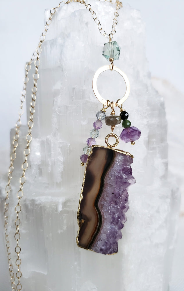 A Raw Amethyst Slice Forms A Charm Drop Pendant Necklace with Various Gemstones Of Fluorite, Green Tourmaline And Amethyst on 14 Kt. Gold-Filled Chain.